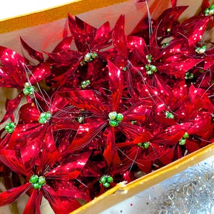 Pu&ograve; includere: Una scatola piena di ornamenti di stella di Natale metallici rossi con centri verdi. Gli ornamenti sono disposti in modo casuale e sono tutti rivolti nella stessa direzione.