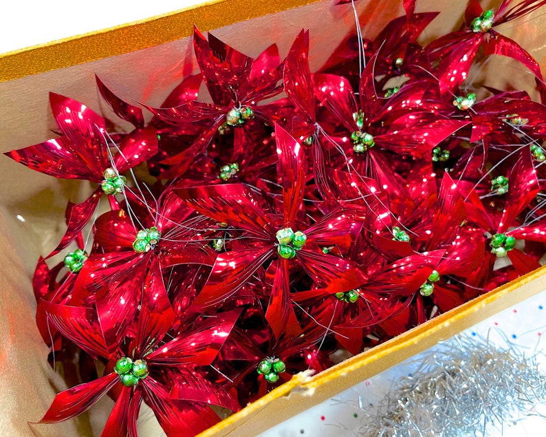 Pu&ograve; includere: Una scatola piena di ornamenti di stella di Natale metallici rossi con centri verdi. Gli ornamenti sono disposti in modo casuale e sono tutti rivolti nella stessa direzione.