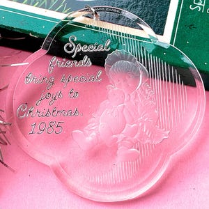 May include: Clear acrylic Christmas ornament with a scalloped edge. The ornament features an etched design of a child holding a teddy bear, with the words "Special friends bring special joys to Christmas. 1985."