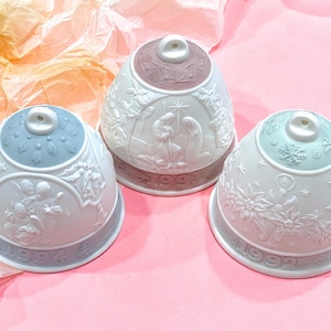 May include: Three white porcelain Christmas bells with different coloured tops. The bells are decorated with raised white designs and the years 1991, 1992, and 1993.