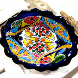 Pode incluir: Uma tigela de cerâmica azul com uma borda ondulada e um design floral colorido. O design apresenta cores amarelas, vermelhas, verdes e azuis.