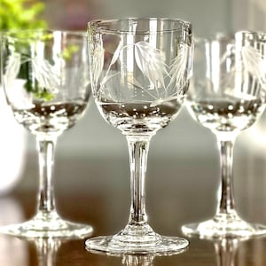 Può includere: Tre bicchieri da liquore in vetro trasparente con disegni di foglie incise. I bicchieri hanno un gambo sottile e una base rotonda. Il disegno inciso è una serie di foglie lunghe e sottili. I bicchieri sono disposti su una superficie riflettente.