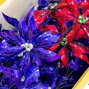 Pu&ograve; includere: Un gruppo di addobbi di stella di Natale metallici blu e rossi. Gli addobbi sono realizzati in lamina lucida e stropicciata e hanno un'atmosfera festosa e natalizia.