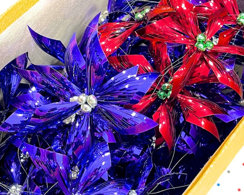 Pu&ograve; includere: Un gruppo di addobbi di stella di Natale metallici blu e rossi. Gli addobbi sono realizzati in lamina lucida e stropicciata e hanno un'atmosfera festosa e natalizia.