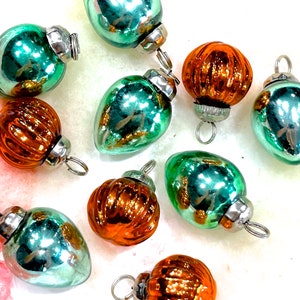 May include: A collection of vintage Christmas ornaments in various shapes and colors. The ornaments are primarily teal and orange, with silver metal caps and hanging loops. Some have a ribbed texture, while others are smooth.