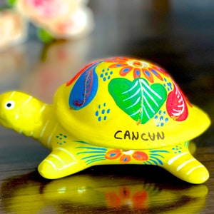 May include: Yellow ceramic turtle with colourful painted designs, including a green heart and the word "CANCUN" on the shell.