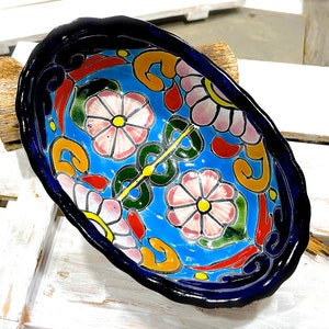 Op de afbeelding: Een blauwe keramische kom met een kleurrijk bloemenmotief. De kom heeft een gegolfde rand en is versierd met roze, gele, groene en rode bloemen.