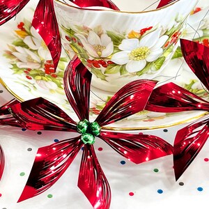 Pu&ograve; includere: Fiocchi metallici rossi e verdi con una tazza da t&egrave; e un piattino in porcellana bianca con motivi floreali.