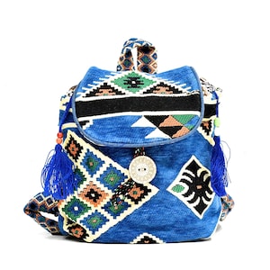 May include: A blue and white patterned backpack with a large button and tassels. The backpack has a geometric design with orange, green, and black accents.