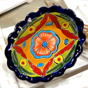 Pode incluir: Uma tigela de cerâmica colorida com uma borda festonada. A tigela é decorada com um desenho floral em tons de vermelho, laranja, amarelo, azul e verde. A tigela é perfeita para servir petiscos, molhos ou saladas.