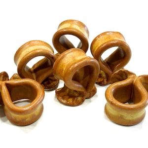 Op de afbeelding: Een set van zes keramische servetringen met een glanzende, warm beige en crèmekleurige glazuurlaag. Elke ring heeft een afgerond, gelust ontwerp met een uitlopende voet, met variaties in de aardse bruintinten op het oppervlak.