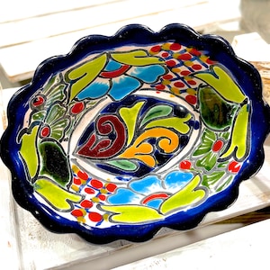 Pode incluir: Uma tigela de cerâmica azul e branca com uma borda ondulada. A tigela é decorada com um padrão floral colorido em tons de vermelho, amarelo, verde e azul.
