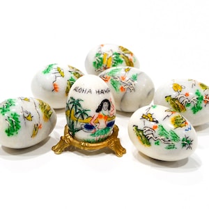 May include: Seven white marble eggs with hand-painted designs, including a hula girl on one egg with the text "Aloha Hawaii".