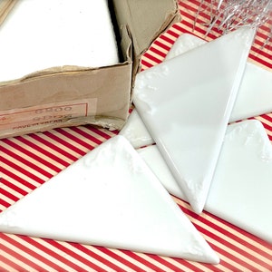 May include: Four white ceramic triangle tiles with a decorative design. The tiles are arranged in a stack on a red and white striped surface. The tiles are labeled "No. 6200 MADE IN JAPAN".