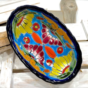 Könnte beinhalten: Eine blaue ovale Servierplatte aus Keramik mit einem farbenfrohen Blumendesign. Die Platte zeigt gelbe, rote, orange und grüne Blumen auf blauem Hintergrund. Der Rand der Platte ist dunkelblau.