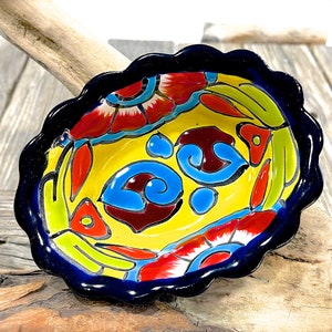 Pode incluir: Uma tigela pequena de cerâmica amarela com uma borda festonada. A tigela é decorada com um padrão floral colorido em tons de vermelho, azul, verde e amarelo. A tigela é perfeita para servir molhos, dips ou petiscos.