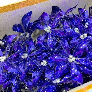 Pu&ograve; includere: Un mazzo di fiocchi metallici blu con centri argentati. I fiocchi sono disposti in una scatola e sono pronti per essere utilizzati per decorare.