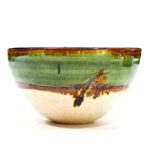 May include: A green and brown ceramic bowl with a white interior. The bowl has a wide rim and a rounded bottom.