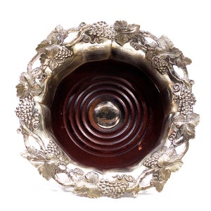 Puede incluir: Porta botellas de vino de plata con diseño de vid y base de madera.