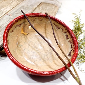 Puede incluir: Un cuenco de cerámica rojo y blanco con un esmalte craquelado. El cuenco está vacío y tiene un borde rojo.
