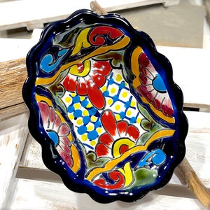 Pode incluir: Uma tigela de cerâmica azul e branca com uma borda ondulada. A tigela é decorada com um padrão floral colorido em tons de vermelho, amarelo, azul e verde.