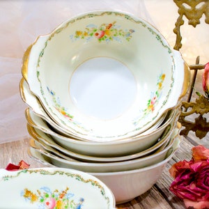 May include: A stack of vintage white porcelain bowls with gold trim and floral designs. The bowls have a scalloped edge and are perfect for serving soup, salad, or dessert.