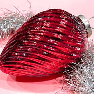 May include: A deep red glass Christmas ornament with a ribbed texture. The ornament has a silver metal cap and loop.