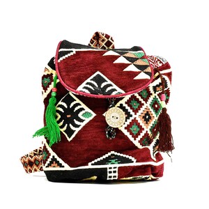 May include: A small, burgundy backpack with a geometric pattern in shades of red, green, and black. The backpack has a flap closure and a decorative button. It features tassels and fringe.