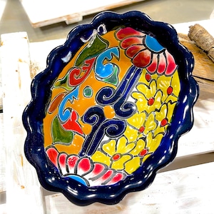 Pode incluir: Uma tigela de cerâmica azul com uma borda ondulada e um design floral colorido. A tigela apresenta flores e redemoinhos amarelos, vermelhos, azuis e verdes.