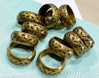 Può includere: Un set di dieci anelli per tovaglioli in metallo dorato con un design intricato e decorativo. Gli anelli sono impilati e disposti in cerchio.