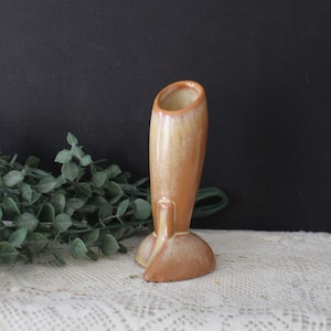 Puede incluir: Un jarrón de cerámica marrón y amarillo con un diseño abstracto único. El jarrón tiene una abertura ancha en la parte superior y una base estrecha.