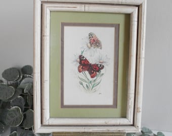 May include: A framed print of two butterflies on white flowers with a green mat and a white distressed frame. The frame is on a gold easel.