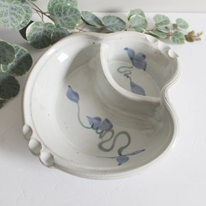 May include: A white ceramic serving dish with two sections. The dish is decorated with a blue and green floral design.