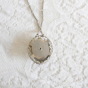 May include: Silver filigree pendant necklace with a round, silver, open back pendant. The pendant has a small hole in the center.