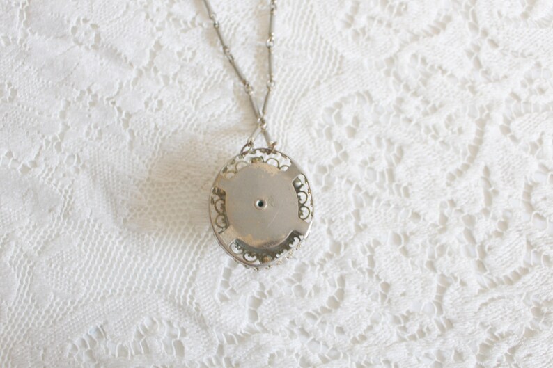 May include: Silver filigree pendant necklace with a round, silver, open back pendant. The pendant has a small hole in the center.