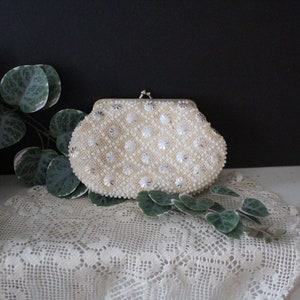 May include: A white beaded clutch purse with a silver clasp. The purse is decorated with small, white beads and silver accents.