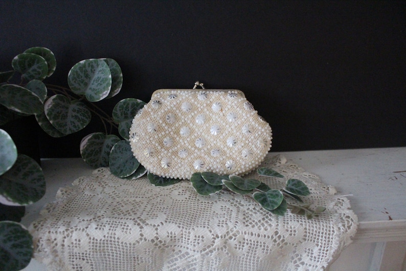 May include: A white beaded clutch purse with a silver clasp. The purse is decorated with small, white beads and silver accents.