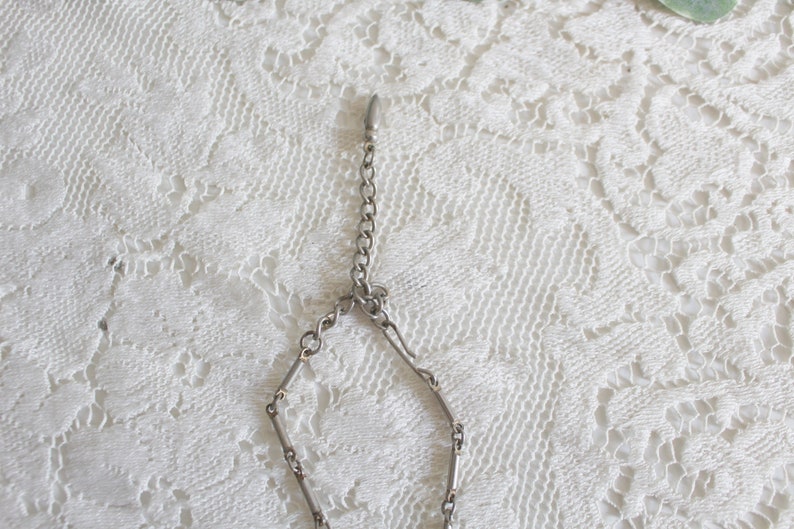 May include: A silver chain necklace with a lobster clasp closure. The chain is made of small, linked bars.
