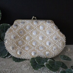 May include: A white beaded clutch purse with a silver floral pattern. The purse has a clasp closure.