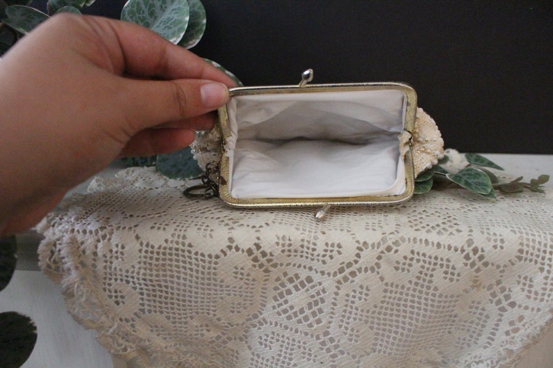 May include: A small, white beaded coin purse with a gold metal frame and a chain attached. The purse is open and the inside is lined with white fabric.
