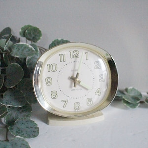 May include: A vintage white alarm clock with gold trim and black hands. The clock face has black numbers and the words "Westclox" and "Time-Rite" printed on it.