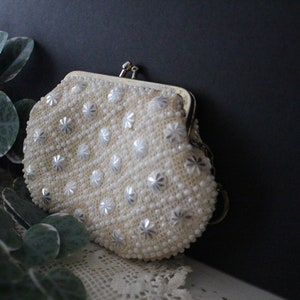 May include: A white beaded clutch purse with a gold clasp. The purse is decorated with silver star-shaped beads.