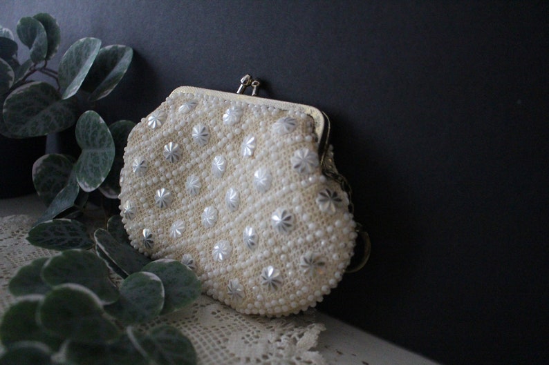 May include: A white beaded clutch purse with a gold clasp. The purse is decorated with silver star-shaped beads.
