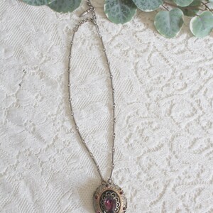 May include: A silver chain necklace with a round pendant featuring a large purple gemstone surrounded by smaller purple gemstones and a gold filigree design.