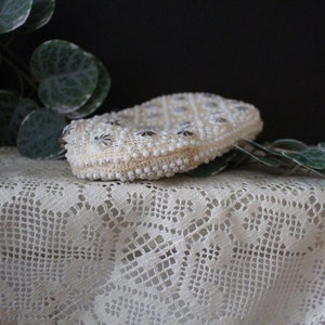 May include: A white beaded clutch purse with a silver clasp. The purse is decorated with a repeating pattern of small silver stars.