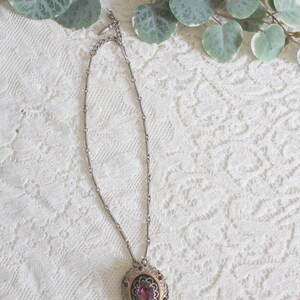 May include: A silver chain necklace with a pendant featuring a large, oval-shaped, purple gemstone surrounded by a gold filigree design and smaller purple gemstones.