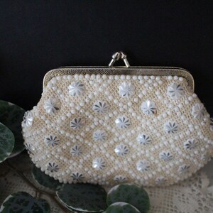May include: A white beaded clutch purse with a silver floral design and a gold clasp.