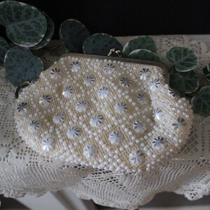 May include: A white beaded clutch purse with a silver clasp. The purse is decorated with white and silver flower-shaped beads.