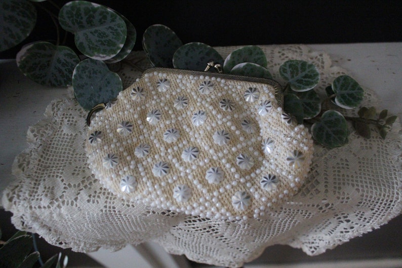 May include: A white beaded clutch purse with a silver clasp. The purse is decorated with white and silver flower-shaped beads.