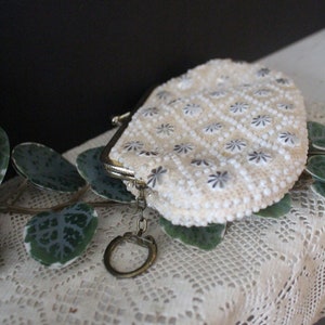 May include: A white beaded coin purse with a silver clasp and a key ring. The purse is on a white crocheted surface.